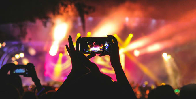 Audience at a concert capturing the colourful stage lights and performance with smartphones.